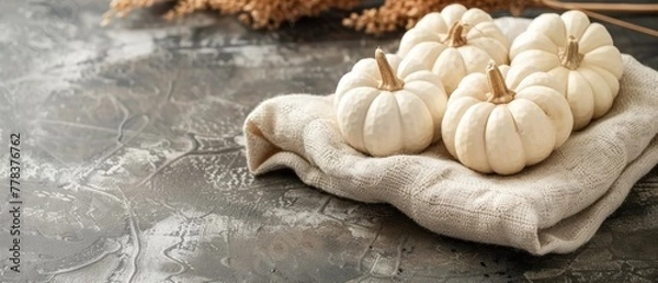 Fototapeta   A cluster of white pumpkins resting atop a cloth on a table