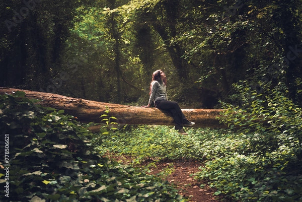 Fototapeta woman sitting on fallen tree in the middle of enchanted and misty forest