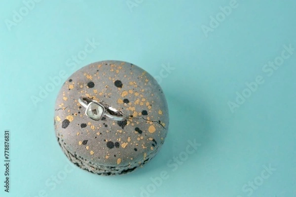 Fototapeta close-up of an engagement silver ring with a gemstone inserted in a grey speckled macaroni cake on an azure background