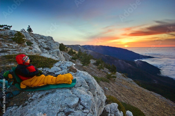 Obraz girl sitting on a cliff in mountains at sunrise