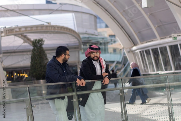 Fototapeta Two arabic males are talking to each other in modern place outdoors like mall shop and huge playing areas about there work life and problems