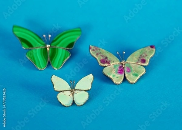 Fototapeta close-up of a set of three colorful butterfly-shaped brooches made of semi-precious stones on a bright blue background