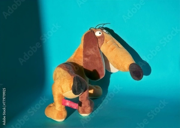 Fototapeta close-up of a half-turn soft toy of a funny light brown dachshund on a blue background with a shadow on the wall