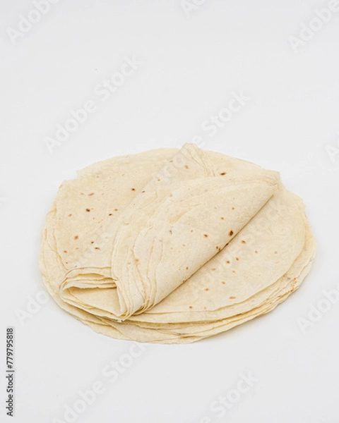 Fototapeta The image shows light-colored, round tortillas stacked on a light-colored background. Round pita bread on a white background