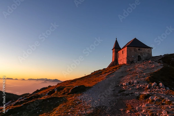 Fototapeta Scenic sunrise view of chapel Maria am Stein on top of mountain peak Dobratsch, Villacher Alps, Austria, Europe. Looking at Julian and Karawanks mountain range. Golden morning hour tranquil atmosphere