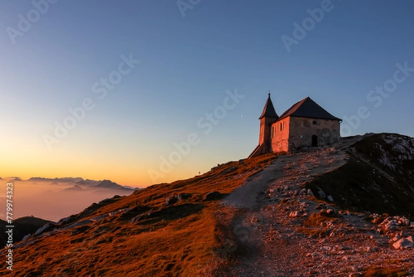 Fototapeta Scenic sunrise view of chapel Maria am Stein on top of mountain peak Dobratsch, Villacher Alps, Austria, Europe. Looking at Julian and Karawanks mountain range. Golden morning hour tranquil atmosphere