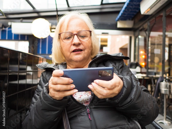 Fototapeta gamer grandmother playing on the mobile phone on a restaurant terrace