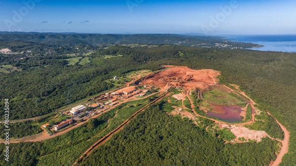 Fototapeta aerial landscape view around a Bauxite mining plant located within a green forest with ocean in the background and orange surface around the mine