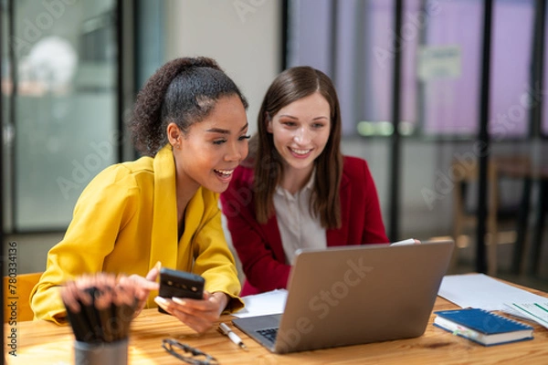 Fototapeta A businesswoman in a yellow blazer engaging in a productive discussion with a colleague in a red jacket over work documents in an office.