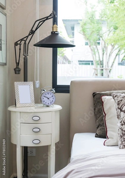 Fototapeta black lamp, picture frame and alarm clock on bedside table