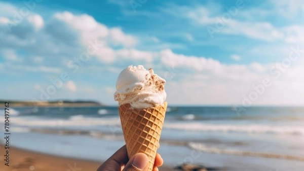 Obraz A hand holding a melting ice cream cone against a sunny beach background.