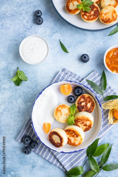 Obraz Cheese pancakes, fritters or syrniki with blueberry, physalis and yogurt, blue background. Healthy and tasty breakfast.