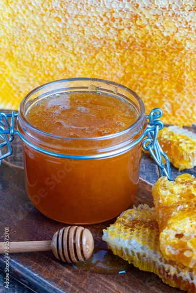 Fototapeta A glass jar of thick golden honey with wooden spoon and honeycombs. Concept of beekeeping, apiculture, apiary. Sweet honey product, healthy food