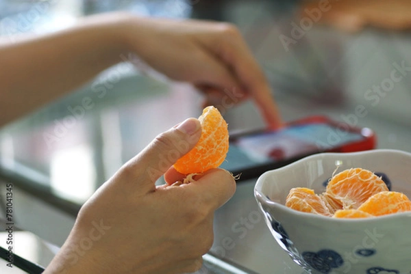 Fototapeta A person eats oranges while playing with a mobile phone, a Relaxing day at home concept