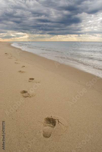Obraz Footprints on a sandy beach, under dark stormy clouds