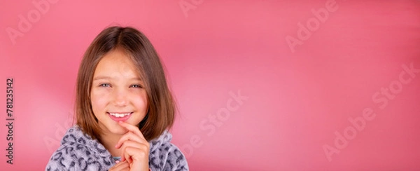 Obraz Portrait or advertising banner with space to insert text and a beautiful smiling little brunette girl 8 years old on a pink background in pajamas close-up