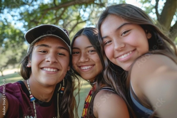Fototapeta Three smiling Native American friends taking a selfie in a park