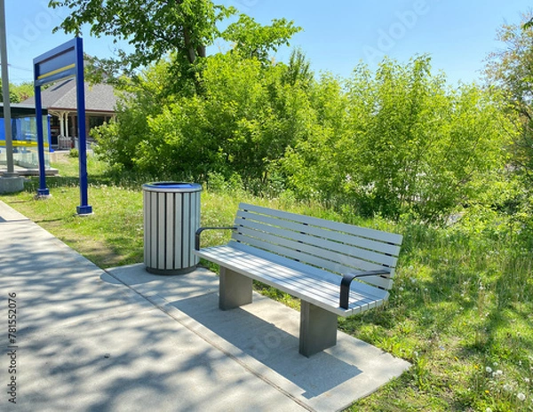 Fototapeta Bench in the park. Public bench in a railway station. Seatings near a litter garbage can. Train station. Furniture for resting while waiting for public transport. 