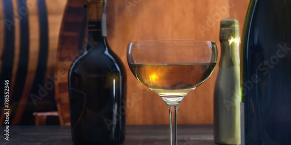 Fototapeta A beautiful semicircular glass with strong alcohol on a background of oak barrels and bottles with elite alcohol