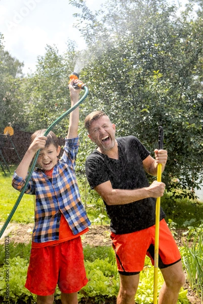 Fototapeta 
happy dad and son are watering plants in the garden. country concept. man and boy taking care of the garden
