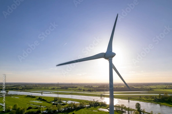 Fototapeta Sun behind wind turbine in The Netherlands part of Dutch 
sustainable industry along river IJssel and Twentekanaal waterway picturesque landscape. Aerial circular economy concept