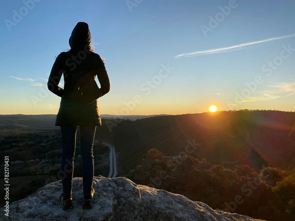 Fototapeta Person on the top of a mountain. Silhouette of a woman looking at the sunset over the blue mountains, NSW, Australia. Spectacular view from a lookout. Hiking to see the sunrise over a grand canyon.