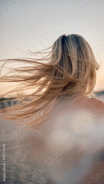 Obraz An evocative scene with a blonde woman's windswept hair by the seaside at golden hour capturing movement and natural beauty