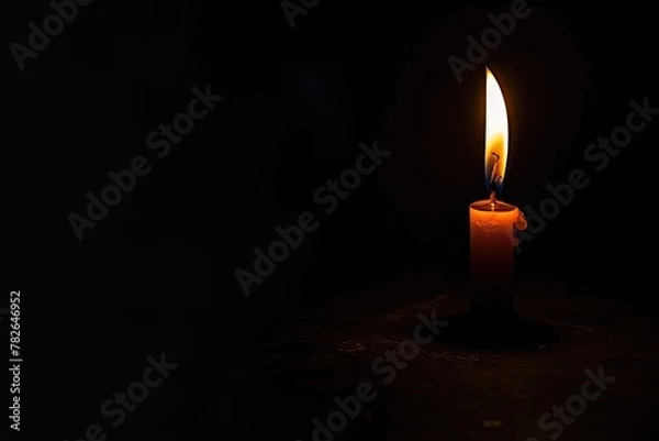 Fototapeta Single candle flame flickering in the vast darkness