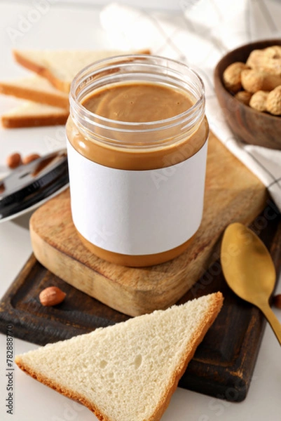 Fototapeta Peanut paste in a glass jar with a spoon, on a light background.