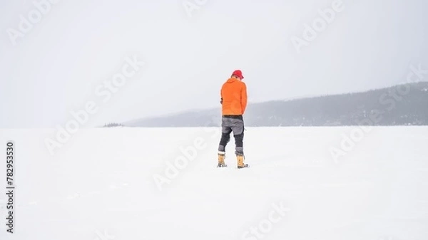 Fototapeta Man with an orange winter Jacket standing on a snow-covered hill