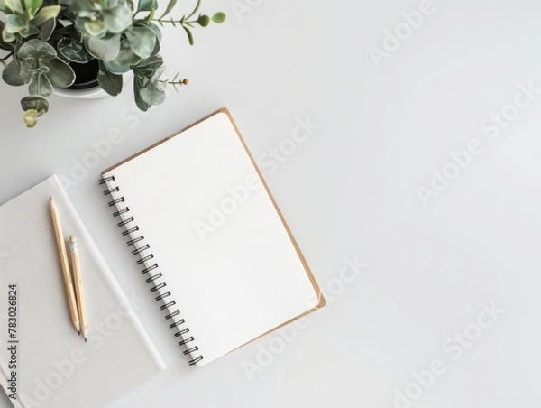Fototapeta A white notebook sits on a table next to a pencil and a potted plant
