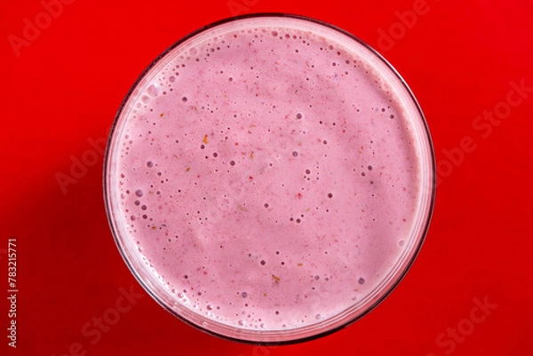 Fototapeta Raspberry banana smoothie in glass on a red background, closeup, top view