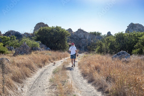 Fototapeta a man walks along a mountain road with a cat on a leash. Travel and Hiking.