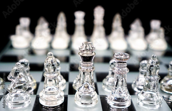 Fototapeta glass chess pieces on chessboard on black background represent competition and strategy concept , selective focus on top of front row pieces