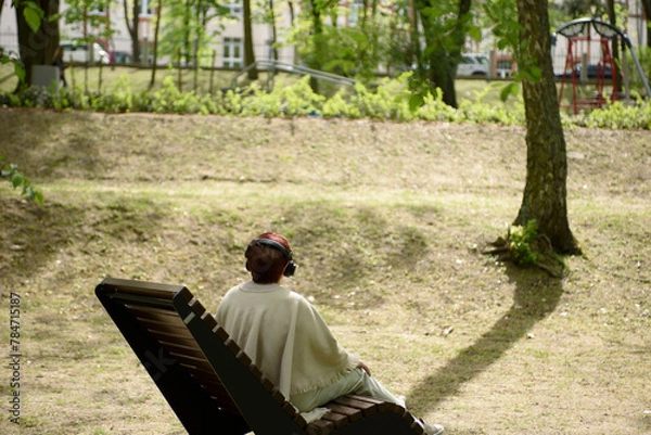 Obraz A woman in the park sits on a bench and listens to music. Millennium Park,  Zielona Gora, Poland 2024.