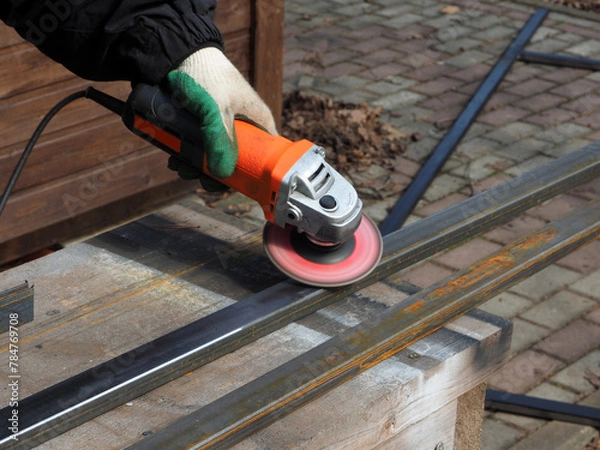 Obraz A worker processes metal with an angle grinder on a construction site.
The concept of locksmith work, processing of metal products.
