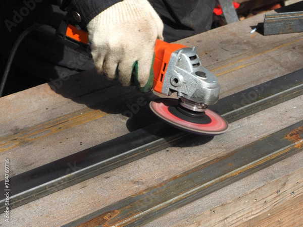 Obraz A worker processes metal with an angle grinder on a construction site.
The concept of locksmith work, processing of metal products.
