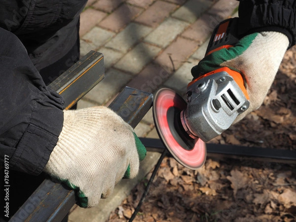 Obraz A worker processes metal with an angle grinder on a construction site.
The concept of locksmith work, processing of metal products.
