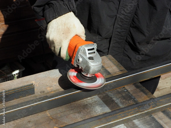 Obraz A worker processes metal with an angle grinder on a construction site.
The concept of locksmith work, processing of metal products.
