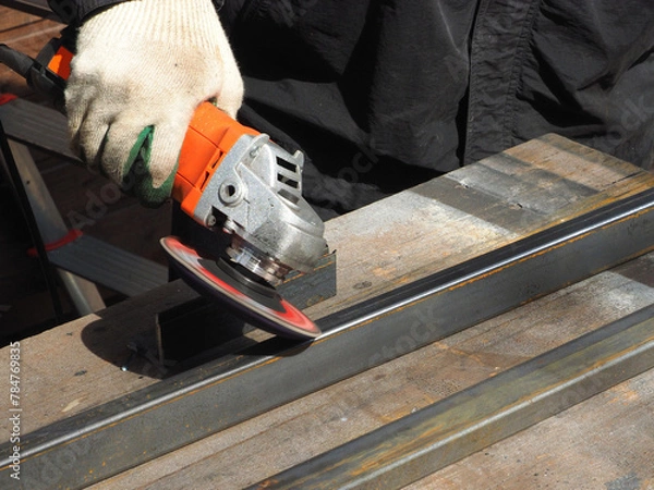 Obraz A worker processes metal with an angle grinder on a construction site.
The concept of locksmith work, processing of metal products.
