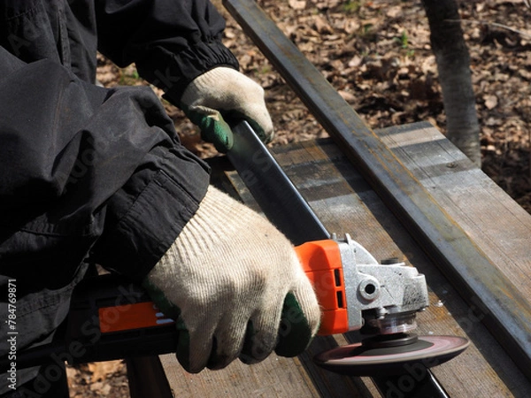 Obraz A worker processes metal with an angle grinder on a construction site.
The concept of locksmith work, processing of metal products.
