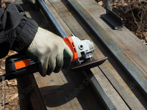 Obraz A worker processes metal with an angle grinder on a construction site.
The concept of locksmith work, processing of metal products.
