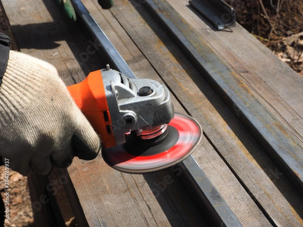 Obraz A worker processes metal with an angle grinder on a construction site.
The concept of locksmith work, processing of metal products.
