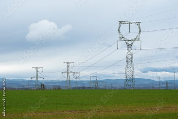 Fototapeta high voltage pylons on a meadow under cloudy skies