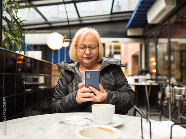 Fototapeta pov senior woman looking at cell phone with coffees already finished