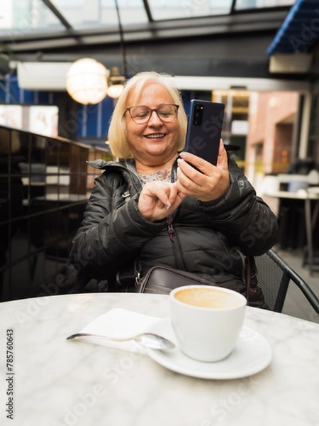 Fototapeta pov senior happy woman enjoying with the cell phone with the coffees already finished