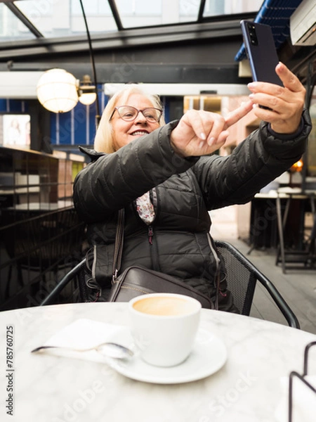 Fototapeta pov senior woman laughing enjoying taking selfie with the cell phone with the coffees already finished
