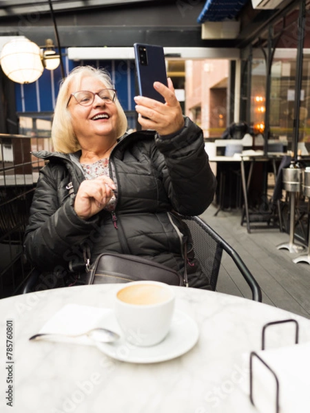 Fototapeta pov senior woman laughing watching selfie with cell phone with already finished coffees