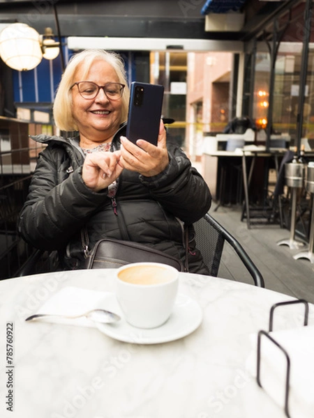Fototapeta pov senior woman laughing sending selfie on cell phone with coffees already finished