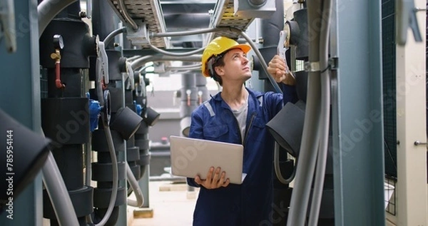 Obraz engineer using laptop checking industry cooling air conditioner water cooling tower air chiller of large industrial building to control air system at construction site